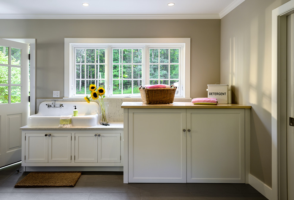 This is an example of a mid-sized country utility room in New York with flat-panel cabinets, white cabinets, marble benchtops, beige walls, ceramic floors and a drop-in sink.