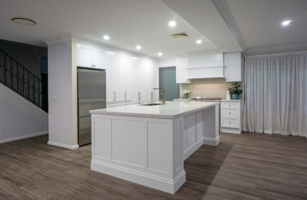 Inspiration for a mid-sized l-shaped dark wood floor and brown floor kitchen pantry remodel in Sydney with a double-bowl sink, shaker cabinets, white cabinets, quartz countertops, beige backsplash, ceramic backsplash, stainless steel appliances, an island and white countertops