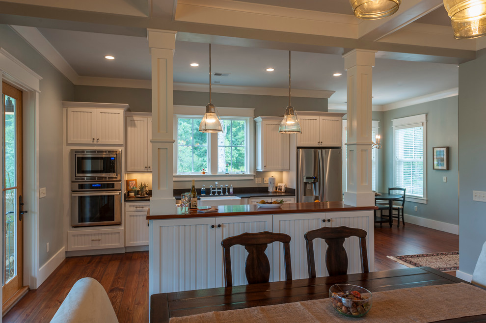 This is an example of a mid-sized country single-wall eat-in kitchen in Charleston with stainless steel appliances, medium hardwood floors, with island, a farmhouse sink, white cabinets, wood benchtops and recessed-panel cabinets.