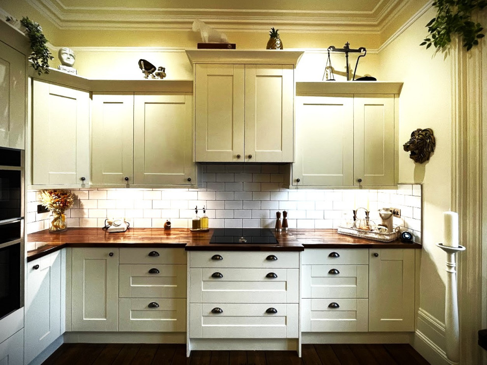 Bild på ett avskilt, mellanstort vintage brun brunt l-kök, med en rustik diskho, skåp i shakerstil, vita skåp, träbänkskiva, vitt stänkskydd, svarta vitvaror, mörkt trägolv, en köksö och brunt golv