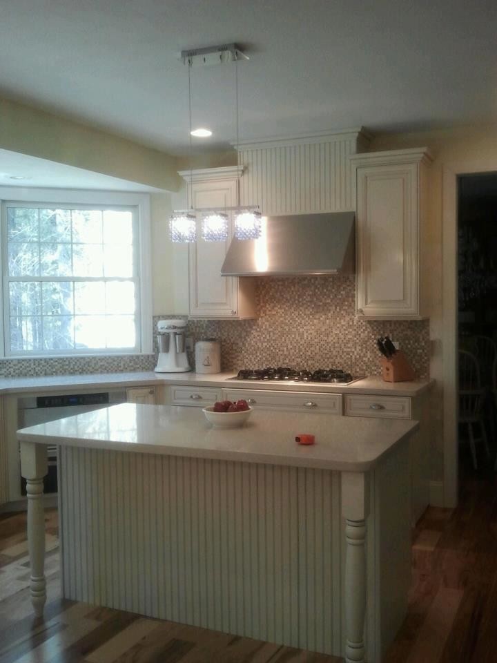 Kitchen - mid-sized medium tone wood floor kitchen idea with raised-panel cabinets, white cabinets, solid surface countertops, gray backsplash, mosaic tile backsplash, stainless steel appliances and an island