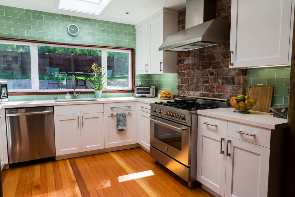 Mid-sized transitional u-shaped open plan kitchen in San Francisco with an undermount sink, shaker cabinets, white cabinets, limestone benchtops, green splashback, glass tile splashback, stainless steel appliances, light hardwood floors and no island.