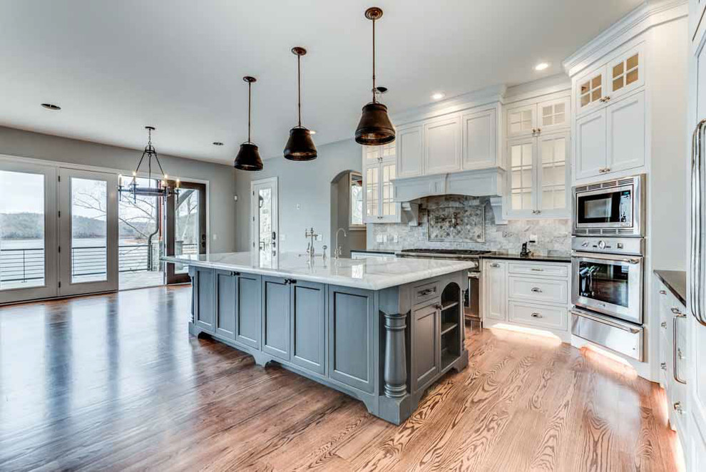 Photo of a large transitional u-shaped eat-in kitchen in Cleveland with a drop-in sink, recessed-panel cabinets, white cabinets, granite benchtops, grey splashback, marble splashback, stainless steel appliances, medium hardwood floors, with island and brown floor.