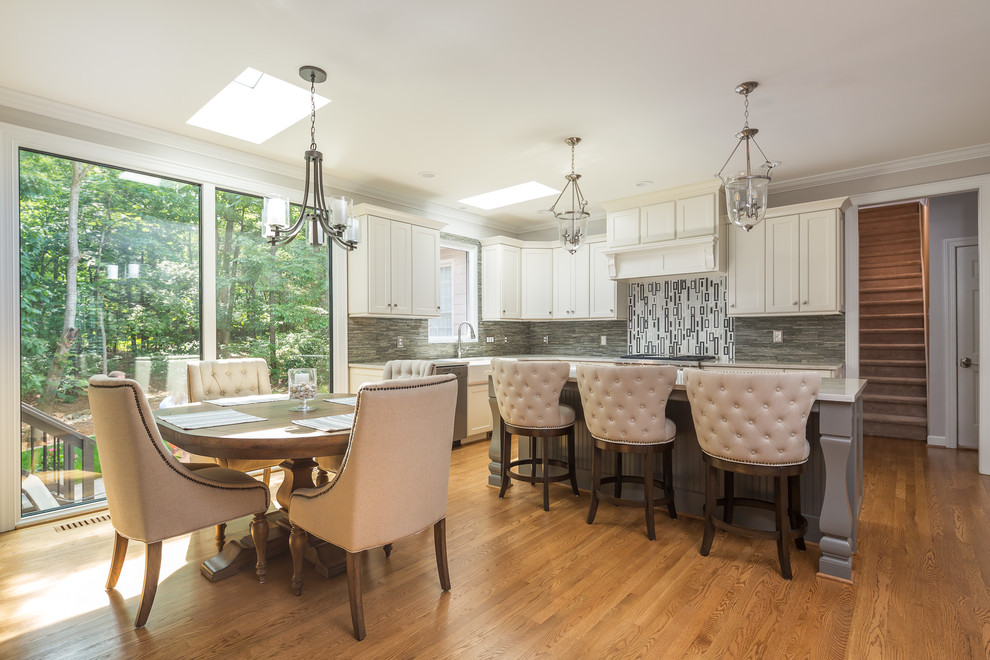 Large transitional l-shaped eat-in kitchen in Raleigh with a farmhouse sink, shaker cabinets, white cabinets, quartzite benchtops, grey splashback, slate splashback, stainless steel appliances, medium hardwood floors, with island, brown floor and white benchtop.