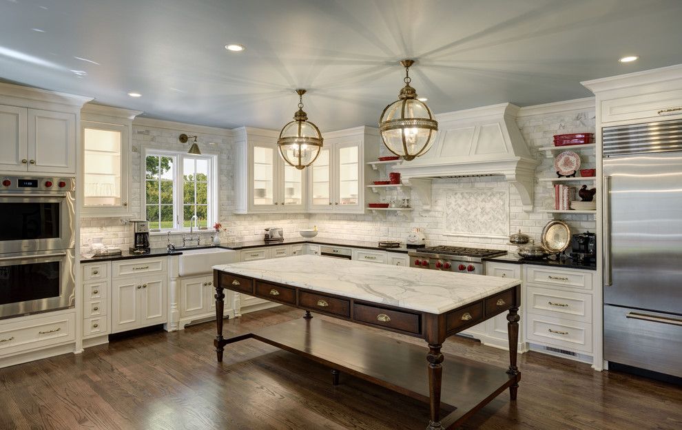 Inspiration for a traditional l-shaped kitchen in Tampa with a farmhouse sink, recessed-panel cabinets, beige cabinets, marble benchtops, grey splashback, marble splashback, stainless steel appliances, dark hardwood floors, with island, brown floor and beige benchtop.
