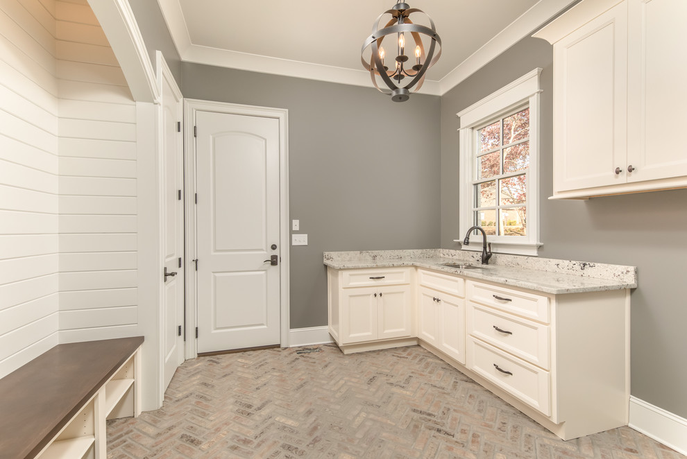 Photo of a mid-sized traditional u-shaped utility room in Other with an undermount sink, recessed-panel cabinets, beige cabinets, granite benchtops, grey walls and brick floors.