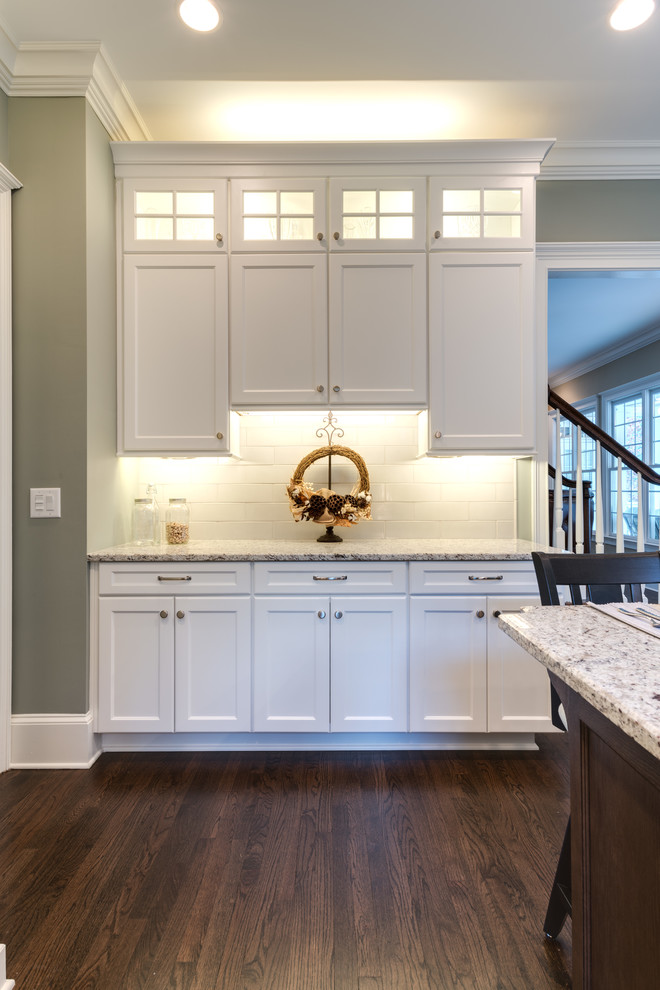 This is an example of an expansive transitional l-shaped eat-in kitchen in Atlanta with an undermount sink, recessed-panel cabinets, white cabinets, granite benchtops, porcelain splashback, stainless steel appliances, dark hardwood floors, with island, white splashback, brown floor and white benchtop.