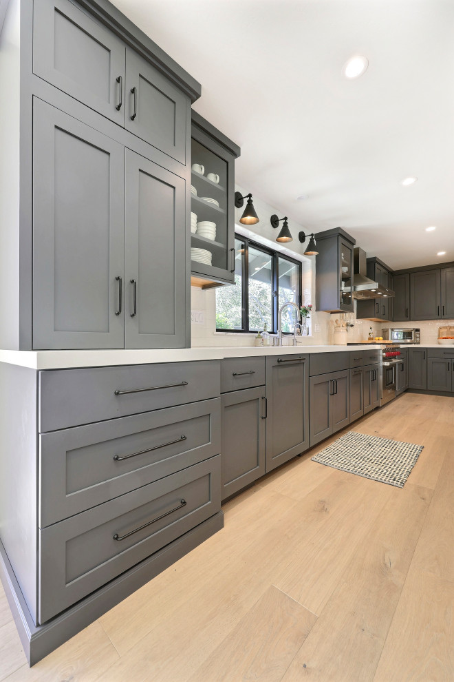 Open concept kitchen - mid-sized transitional l-shaped laminate floor open concept kitchen idea with a double-bowl sink, flat-panel cabinets, gray cabinets, quartz countertops, white backsplash, ceramic backsplash, stainless steel appliances, an island and white countertops