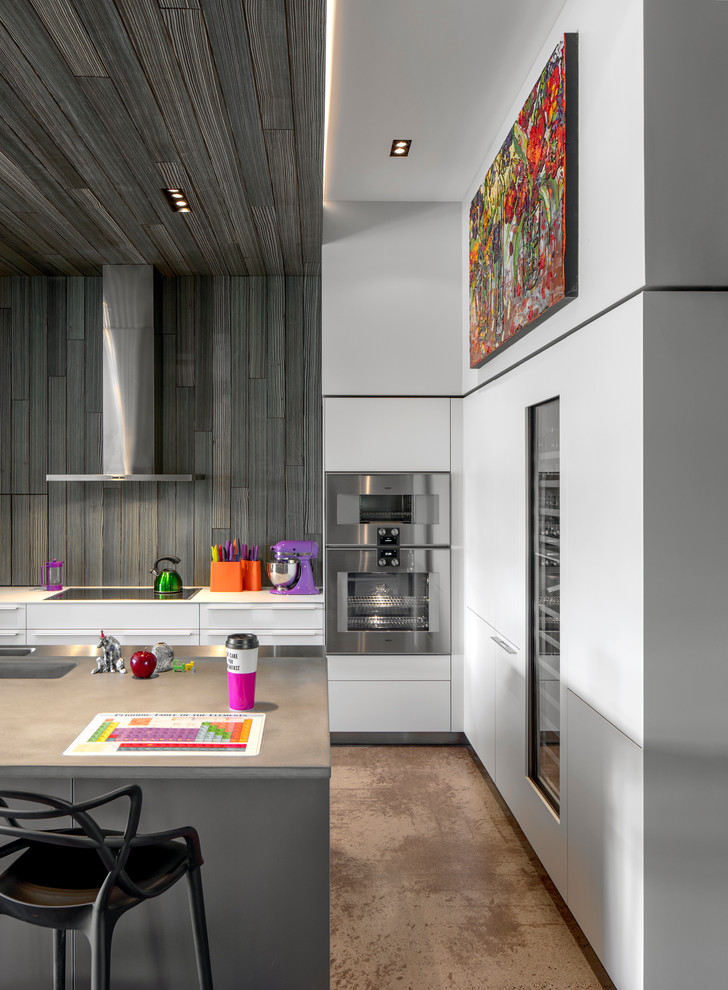 Contemporary l-shaped kitchen in Phoenix with an undermount sink, flat-panel cabinets, white cabinets, grey splashback, stainless steel appliances, concrete floors, with island, brown floor and grey benchtop.