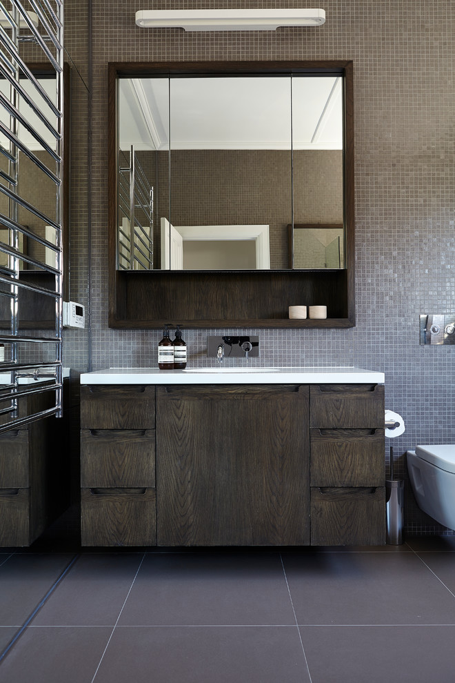 This is an example of a mid-sized contemporary bathroom in Melbourne with flat-panel cabinets, dark wood cabinets, a wall-mount toilet, brown tile, mosaic tile, brown walls and white benchtops.