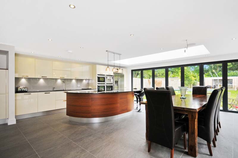 This is an example of a large modern galley eat-in kitchen in London with a double-bowl sink, grey cabinets, wood benchtops, brown splashback and coloured appliances.