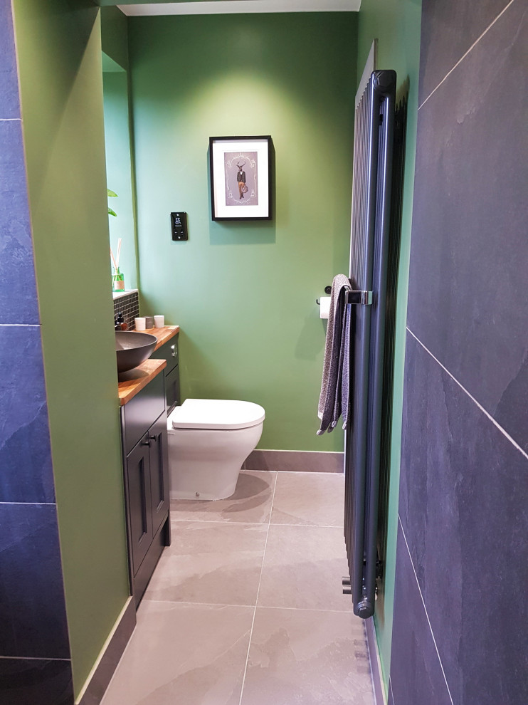 Foto på ett litet funkis flerfärgad badrum för barn, med skåp i shakerstil, blå skåp, våtrum, en toalettstol med hel cisternkåpa, svart kakel, porslinskakel, gröna väggar, klinkergolv i porslin, ett fristående handfat, träbänkskiva, grått golv och med dusch som är öppen