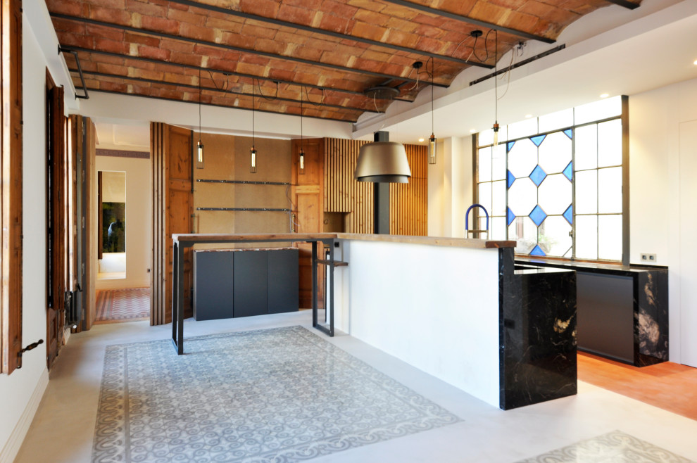 This is an example of a large modern single-wall open plan kitchen in Barcelona with an integrated sink, flat-panel cabinets, grey cabinets, granite benchtops, black splashback, granite splashback, panelled appliances, terra-cotta floors, with island, red floor, black benchtop and vaulted.