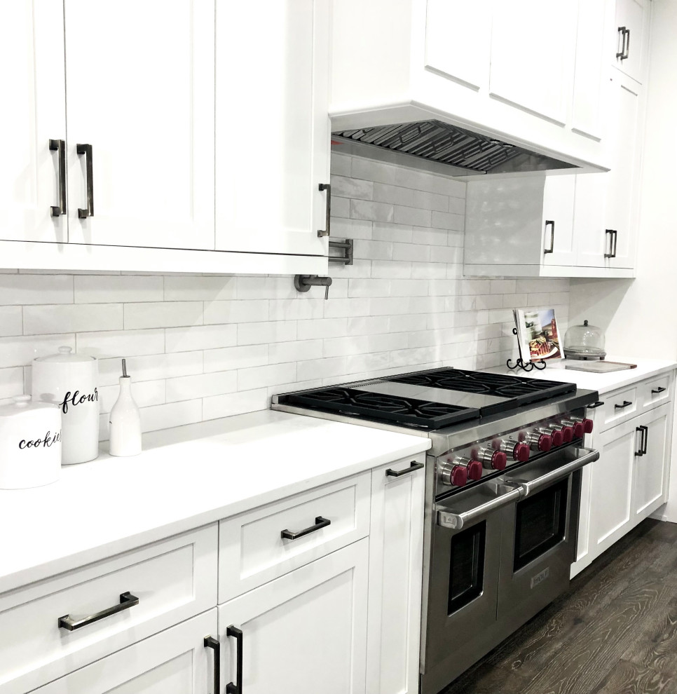 Moderne Küche mit Schrankfronten im Shaker-Stil, Quarzit-Arbeitsplatte, Küchenrückwand in Weiß, Rückwand aus Metrofliesen, Küchengeräten aus Edelstahl, dunklem Holzboden, Kücheninsel, grauem Boden und weißer Arbeitsplatte in Atlanta