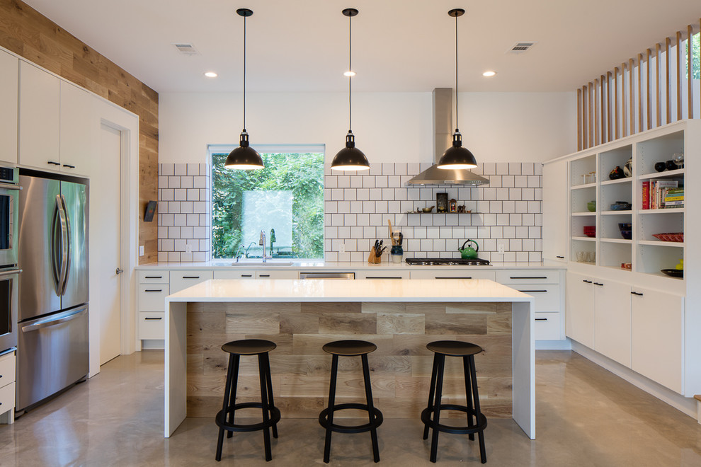 Photo of a mid-sized country u-shaped open plan kitchen in Austin with an undermount sink, flat-panel cabinets, white cabinets, white splashback, stainless steel appliances, concrete floors, with island, solid surface benchtops, porcelain splashback and white benchtop.