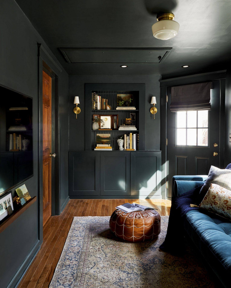 Design ideas for a mid-sized transitional enclosed living room in Detroit with a library, black walls, medium hardwood floors, no fireplace, a wall-mounted tv, brown floor and decorative wall panelling.