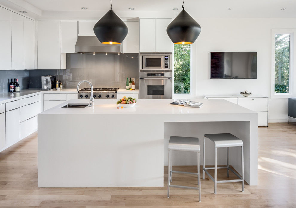Design ideas for a large contemporary l-shaped open plan kitchen in Seattle with an undermount sink, flat-panel cabinets, white cabinets, solid surface benchtops, grey splashback, stainless steel appliances, light hardwood floors, with island and beige floor.