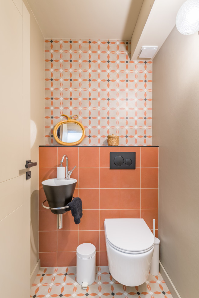 Immagine di un bagno di servizio nordico con WC sospeso, piastrelle multicolore, piastrelle in ceramica, pareti beige, pavimento con piastrelle in ceramica, lavabo sospeso e pavimento multicolore