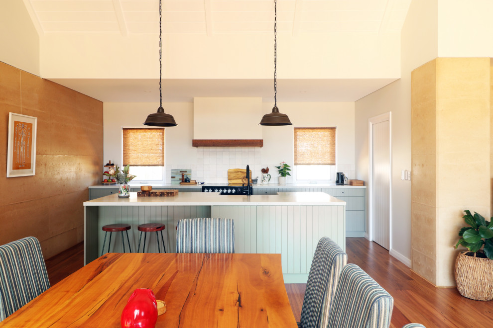 Mid-sized contemporary open plan kitchen in Other with a farmhouse sink, green cabinets, white splashback, ceramic splashback, black appliances, medium hardwood floors, with island and white benchtop.
