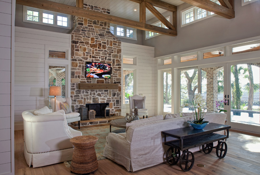 Inspiration for a large tropical formal open concept living room in Atlanta with white walls, medium hardwood floors, a standard fireplace, a stone fireplace surround and a wall-mounted tv.
