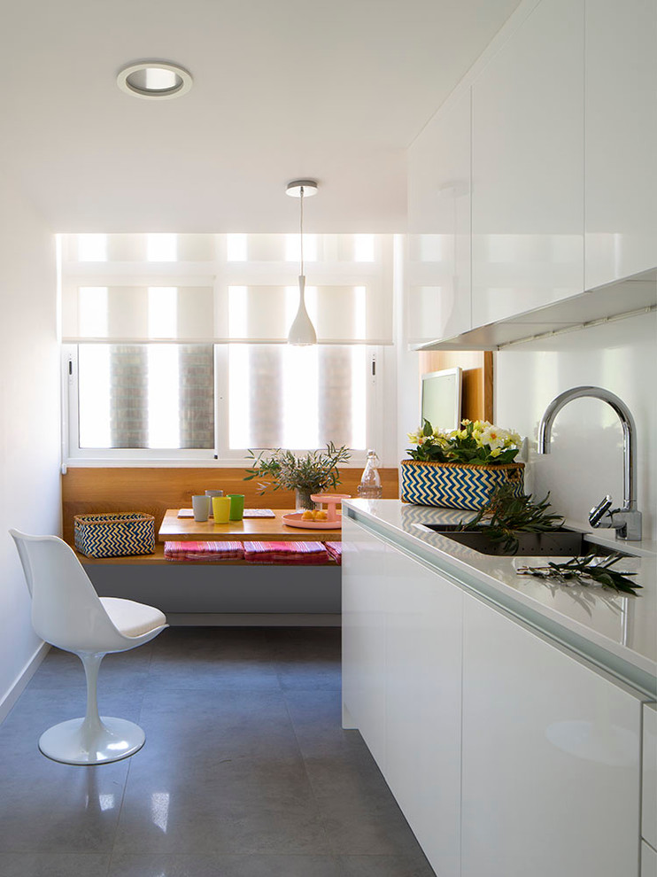 This is an example of a mid-sized scandinavian single-wall eat-in kitchen in Other with an undermount sink, flat-panel cabinets, white cabinets, solid surface benchtops, white splashback, stainless steel appliances, concrete floors, no island and white benchtop.