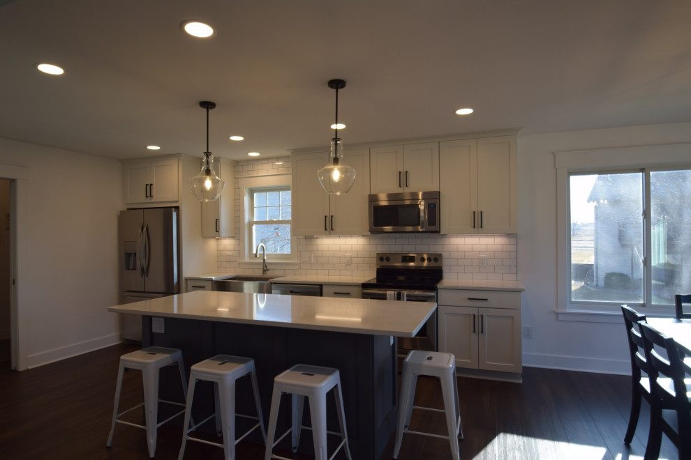 Example of a mid-sized transitional single-wall vinyl floor open concept kitchen design with a farmhouse sink, shaker cabinets, quartz countertops, white backsplash, subway tile backsplash, stainless steel appliances, an island and white countertops