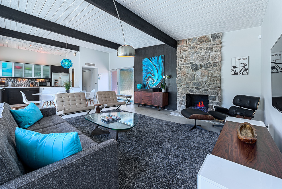 Midcentury living room in Other with white walls, concrete floors, a stone fireplace surround and a wall-mounted tv.