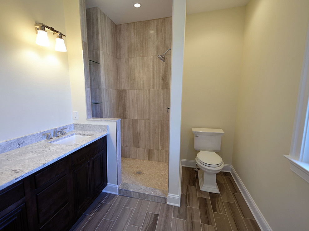 Photo of a mid-sized beach style master bathroom in Other with an undermount sink, raised-panel cabinets, dark wood cabinets, granite benchtops, a freestanding tub, an open shower, a one-piece toilet, gray tile, ceramic tile, yellow walls and ceramic floors.