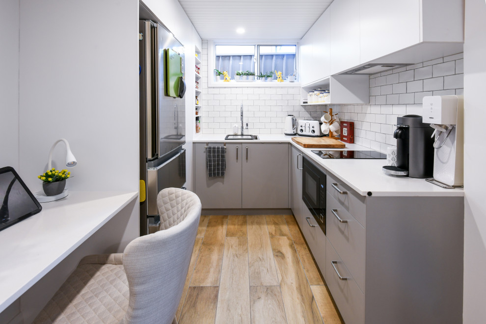 Photo of a small contemporary u-shaped eat-in kitchen in Sydney with a single-bowl sink, flat-panel cabinets, grey cabinets, quartz benchtops, white splashback, subway tile splashback, stainless steel appliances, ceramic floors, no island, brown floor and white benchtop.
