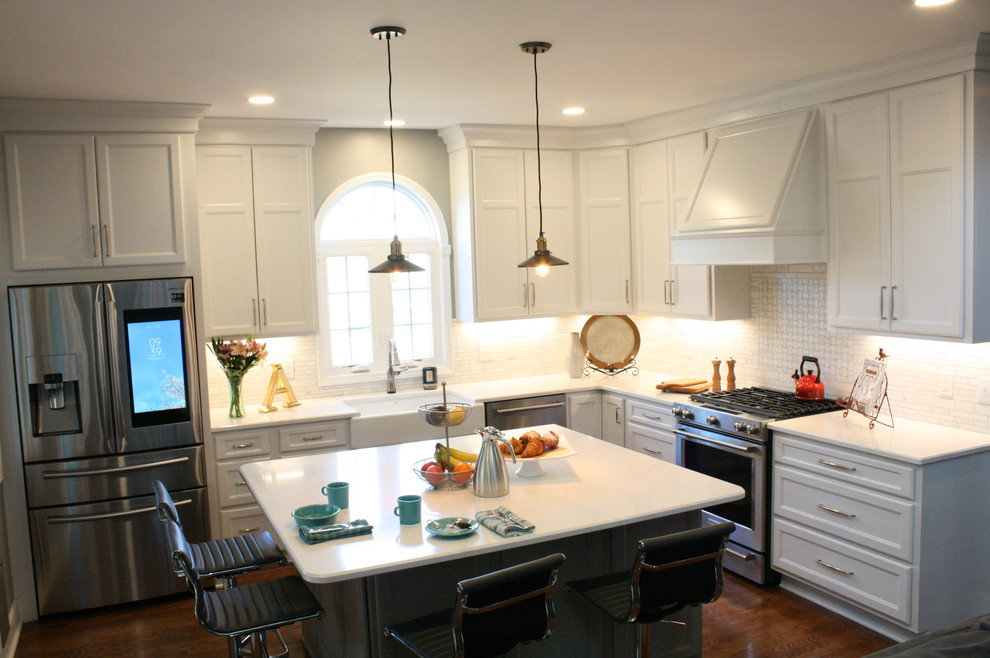 Example of a transitional dark wood floor and brown floor kitchen design in Nashville with a farmhouse sink, flat-panel cabinets, white cabinets, white backsplash, stainless steel appliances, an island and white countertops