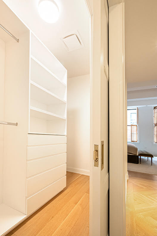 Cette photo montre un dressing moderne de taille moyenne et neutre avec un placard à porte plane, des portes de placard blanches, un sol en bois brun, un sol marron et un plafond voûté.