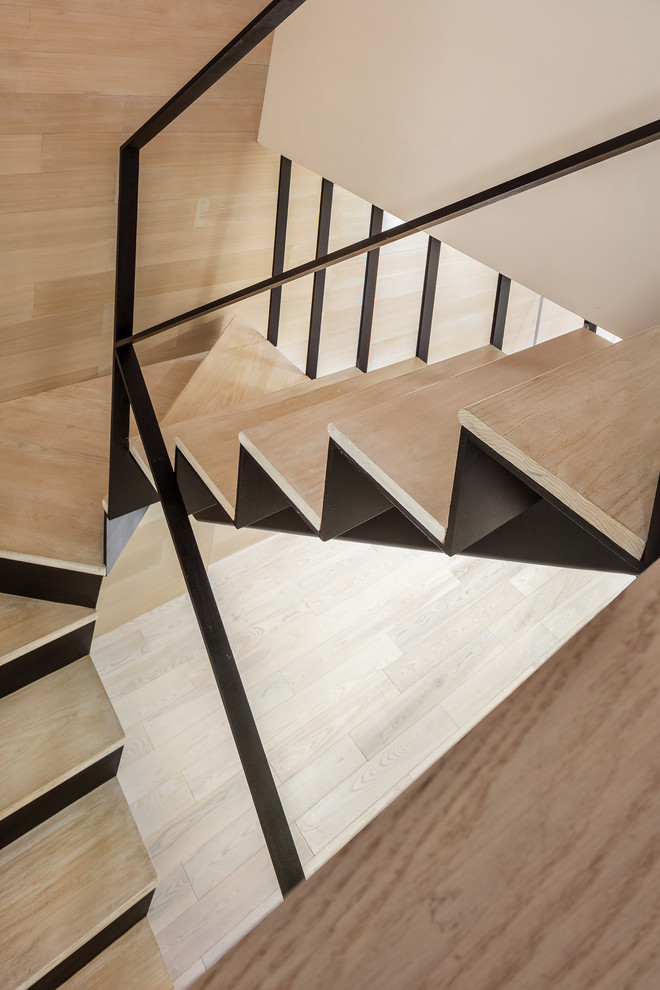 This is an example of a large contemporary wood u-shaped staircase in New York with metal risers and metal railing.