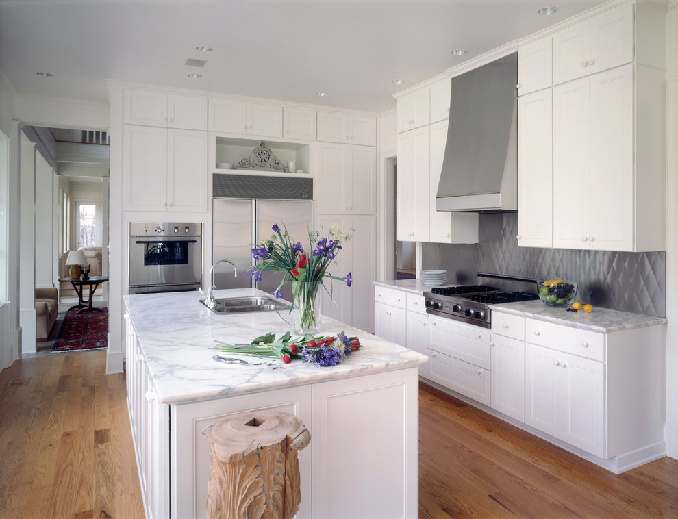 Design ideas for a traditional l-shaped eat-in kitchen in DC Metro with a double-bowl sink, recessed-panel cabinets, white cabinets, marble benchtops, metallic splashback, stainless steel appliances and light hardwood floors.
