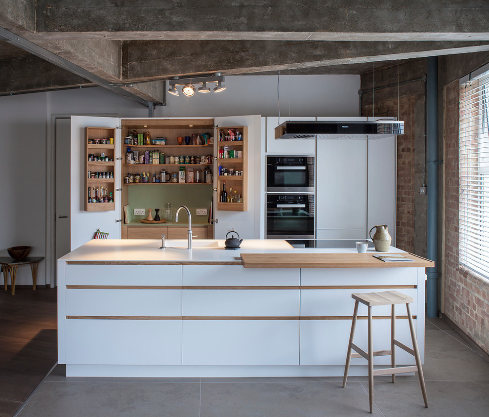 Industrial galley open plan kitchen in London with white cabinets, solid surface benchtops, black appliances, with island, an integrated sink and flat-panel cabinets.