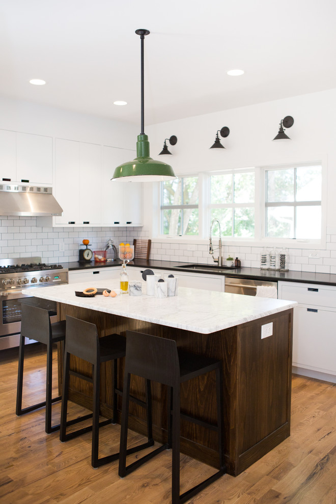 This is an example of a country l-shaped kitchen in Minneapolis with an undermount sink, white splashback, subway tile splashback, stainless steel appliances, medium hardwood floors and with island.