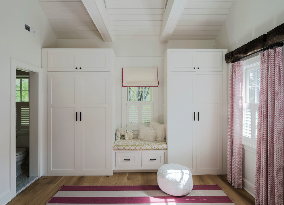 This is an example of a large country bedroom in New York with white walls, medium hardwood floors and no fireplace.