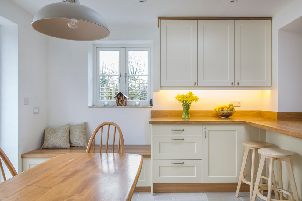 Photo of a transitional kitchen in Oxfordshire with flat-panel cabinets, wood benchtops and travertine floors.