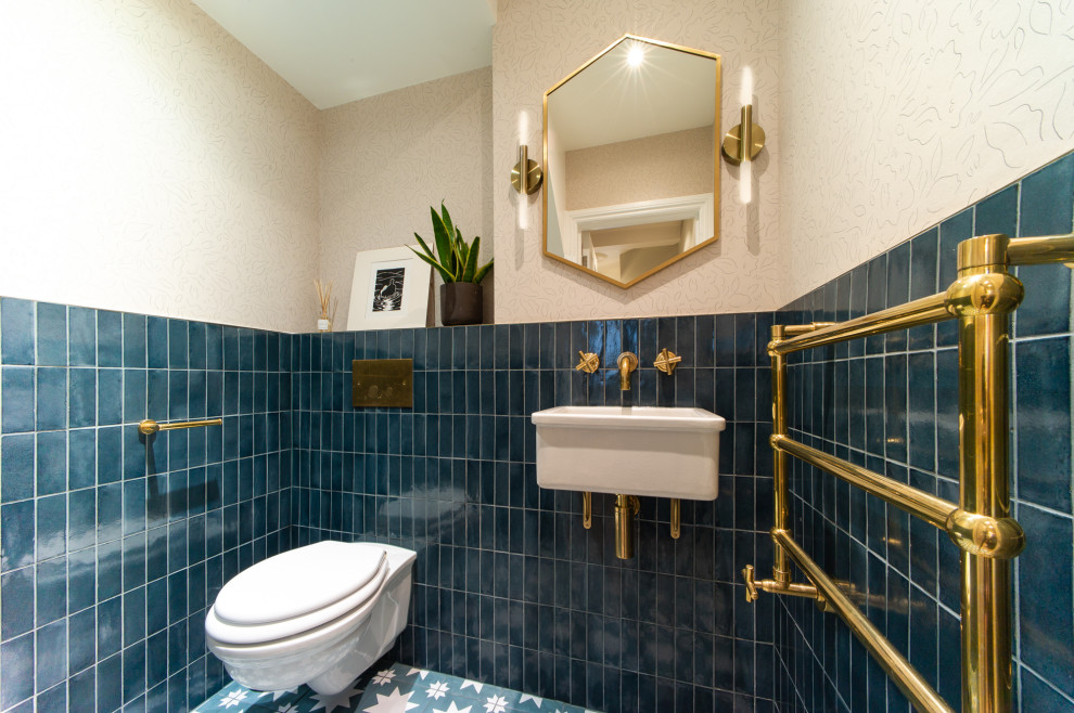 Design ideas for a mid-sized transitional powder room in London with a wall-mount toilet, blue tile, porcelain tile, porcelain floors, a wall-mount sink, blue floor, wallpaper and pink walls.