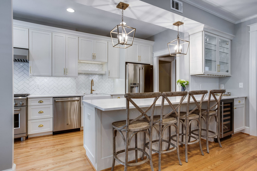 Eat-in kitchen - mid-sized transitional galley light wood floor and beige floor eat-in kitchen idea in DC Metro with a farmhouse sink, shaker cabinets, white cabinets, quartz countertops, white backsplash, subway tile backsplash, stainless steel appliances, a peninsula and white countertops