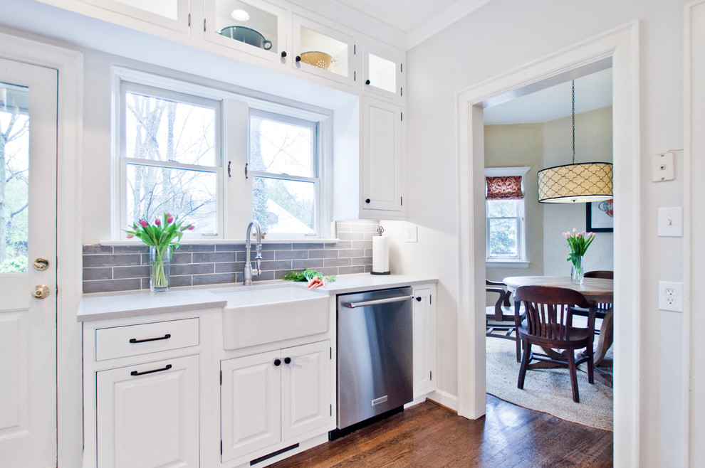 This is an example of a mid-sized transitional u-shaped separate kitchen in Nashville with a farmhouse sink, beaded inset cabinets, white cabinets, quartz benchtops, grey splashback, subway tile splashback, stainless steel appliances, medium hardwood floors, no island, brown floor and grey benchtop.