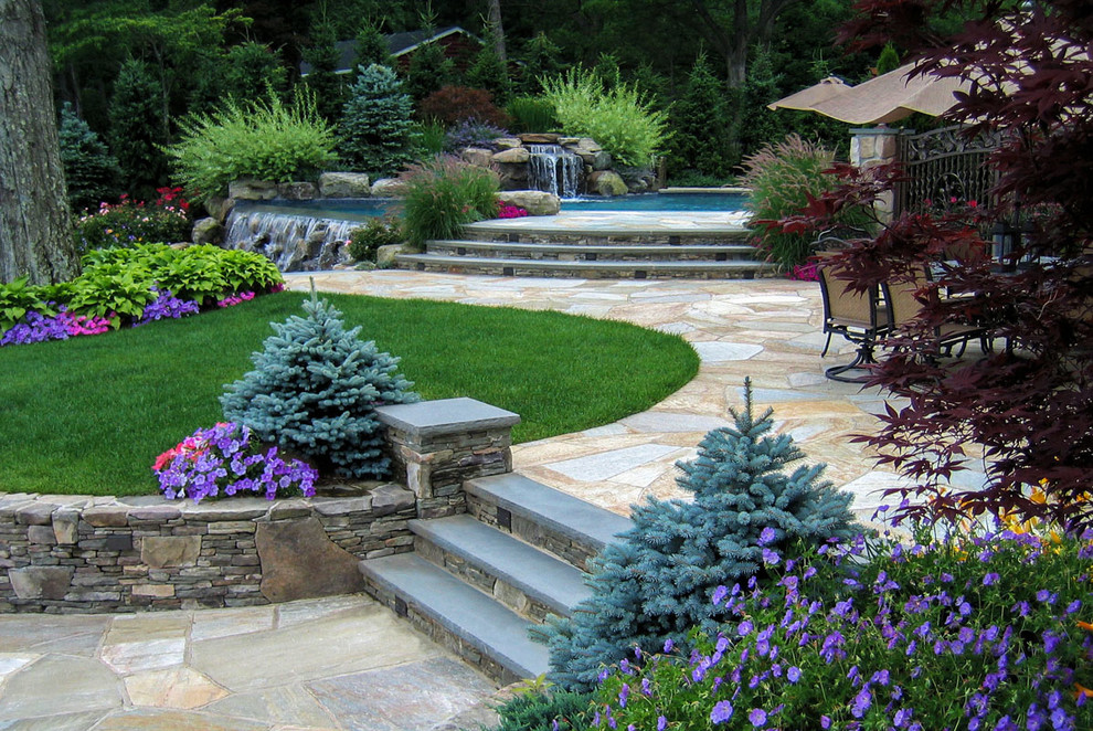 Photo of a large beach style backyard formal garden in New York with natural stone pavers and a retaining wall.