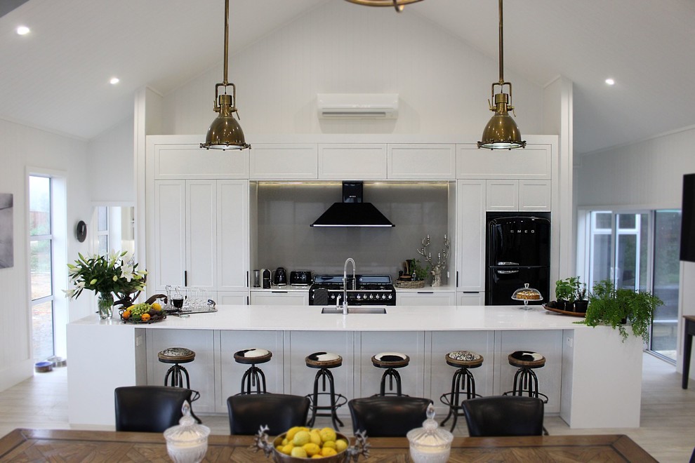 Inspiration for a mid-sized country galley eat-in kitchen in Auckland with an undermount sink, shaker cabinets, white cabinets, grey splashback, glass sheet splashback, black appliances, with island, beige floor and white benchtop.