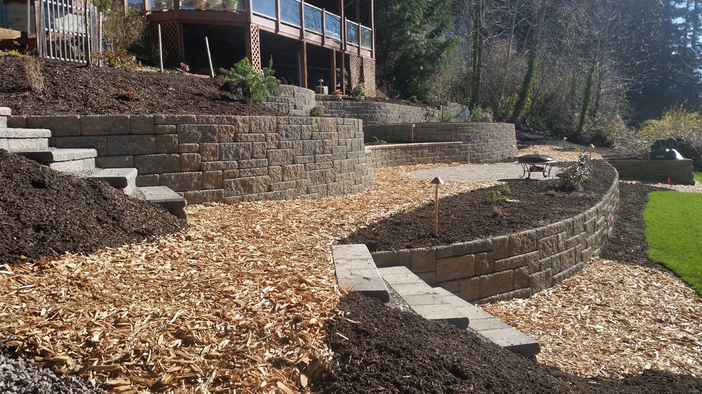 This is an example of a large traditional sloped partial sun garden in Seattle with a retaining wall and natural stone pavers.