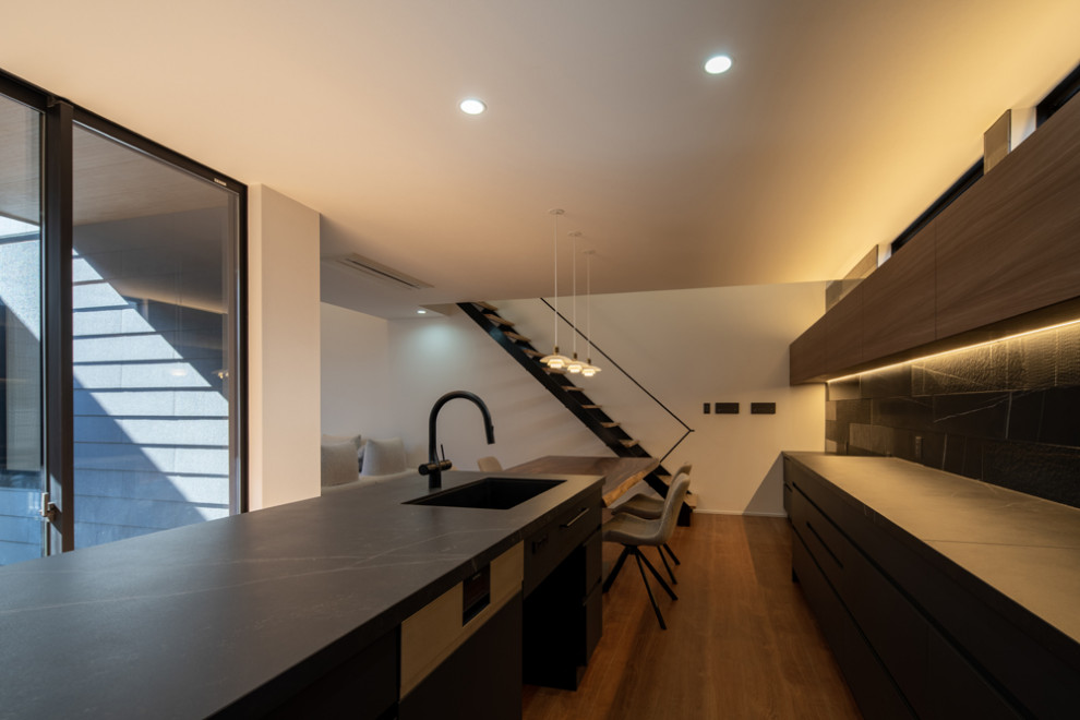 Photo of a large contemporary galley open plan kitchen in Other with an undermount sink, beaded inset cabinets, black cabinets, solid surface benchtops, black splashback, shiplap splashback, painted wood floors, with island, brown floor, black benchtop and wallpaper.
