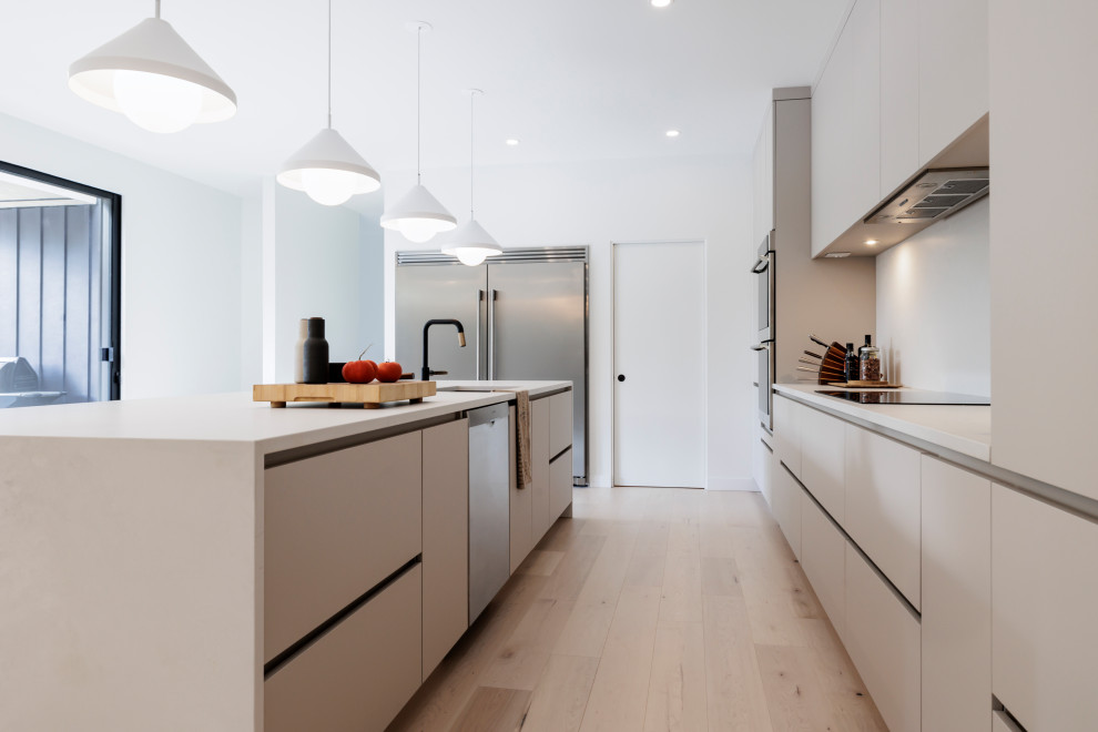 Design ideas for a large scandinavian galley open plan kitchen in New York with an undermount sink, flat-panel cabinets, beige cabinets, quartz benchtops, beige splashback, engineered quartz splashback, stainless steel appliances, painted wood floors, with island and white benchtop.