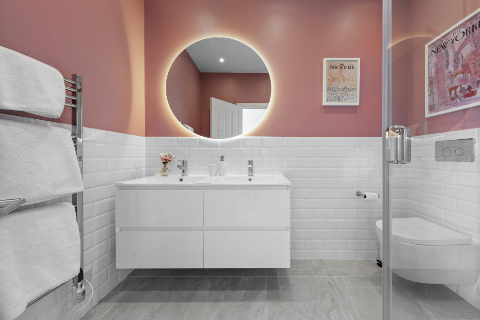 Design ideas for a mid-sized contemporary master bathroom in London with flat-panel cabinets, white cabinets, a corner shower, a wall-mount toilet, white tile, subway tile, pink walls, ceramic floors, grey floor, a hinged shower door, white benchtops, a double vanity and a floating vanity.