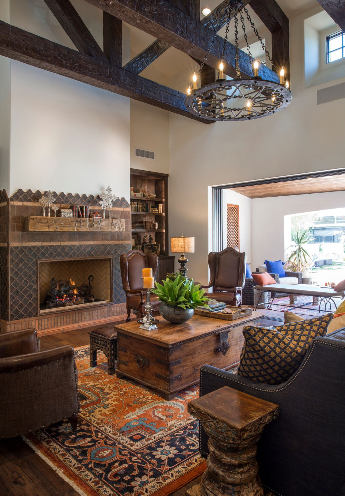 Inspiration for a large mediterranean open concept family room in Phoenix with white walls, dark hardwood floors, a standard fireplace, a tile fireplace surround, a wall-mounted tv and brown floor.