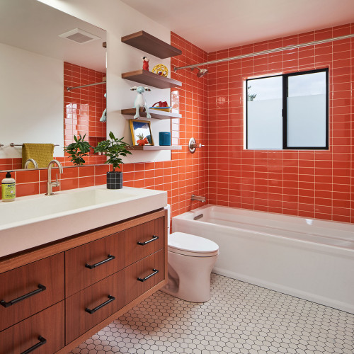 Modern floating wooden bathroom cabinets with white countertop and undermount sink, set against bold orange tile walls in a contemporary bathroom