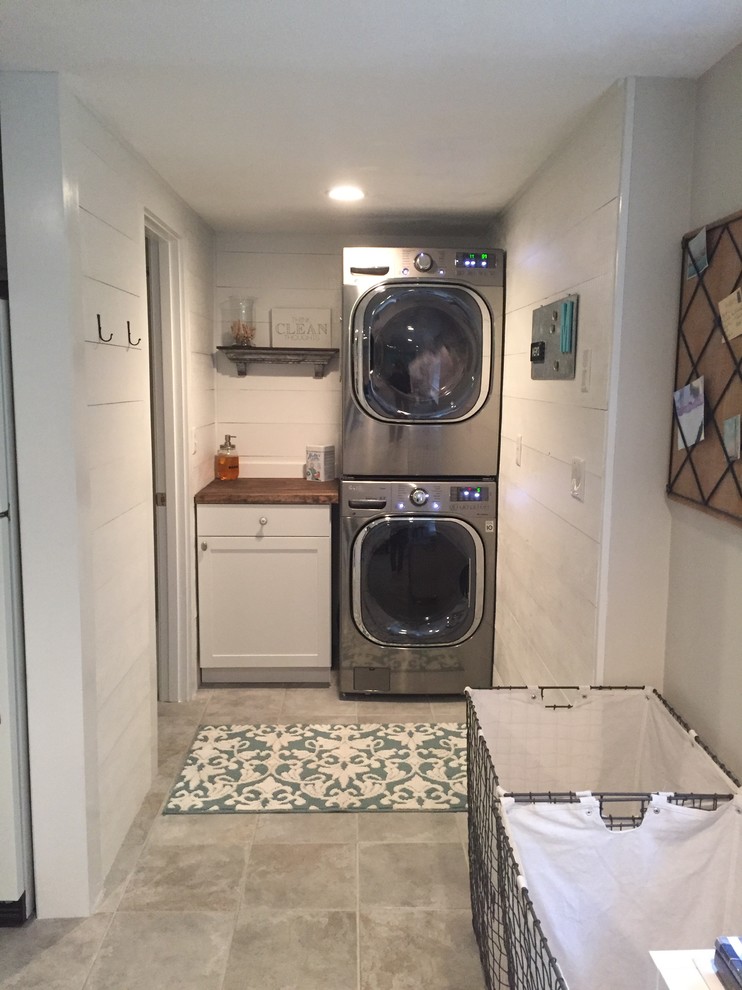 Inspiration for a small u-shaped utility room in Boston with flat-panel cabinets, white cabinets, wood benchtops, white walls, travertine floors, a stacked washer and dryer and grey floor.