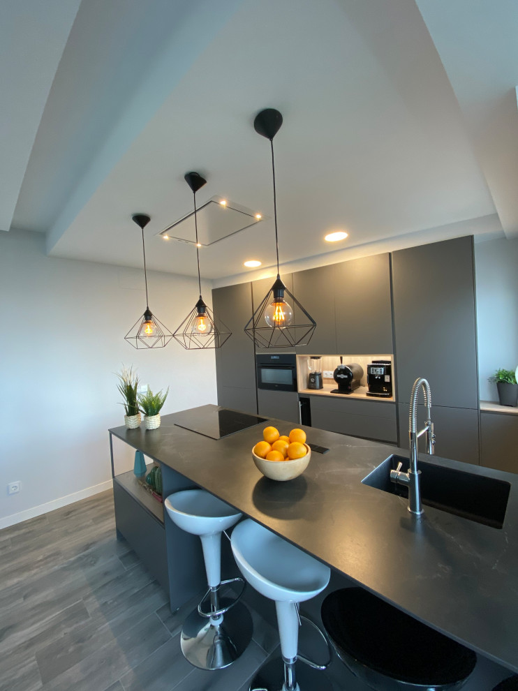 Diseño de cocina lineal contemporánea de tamaño medio abierta con fregadero bajoencimera, armarios con paneles lisos, puertas de armario negras, encimera de cuarzo compacto, electrodomésticos negros, suelo laminado, una isla, suelo marrón y encimeras negras